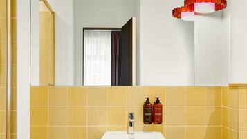 A bathroom with yellow tiles, a white sink, and a red pendant light. There are two bottles on the wall and a towel hanging on the rack.