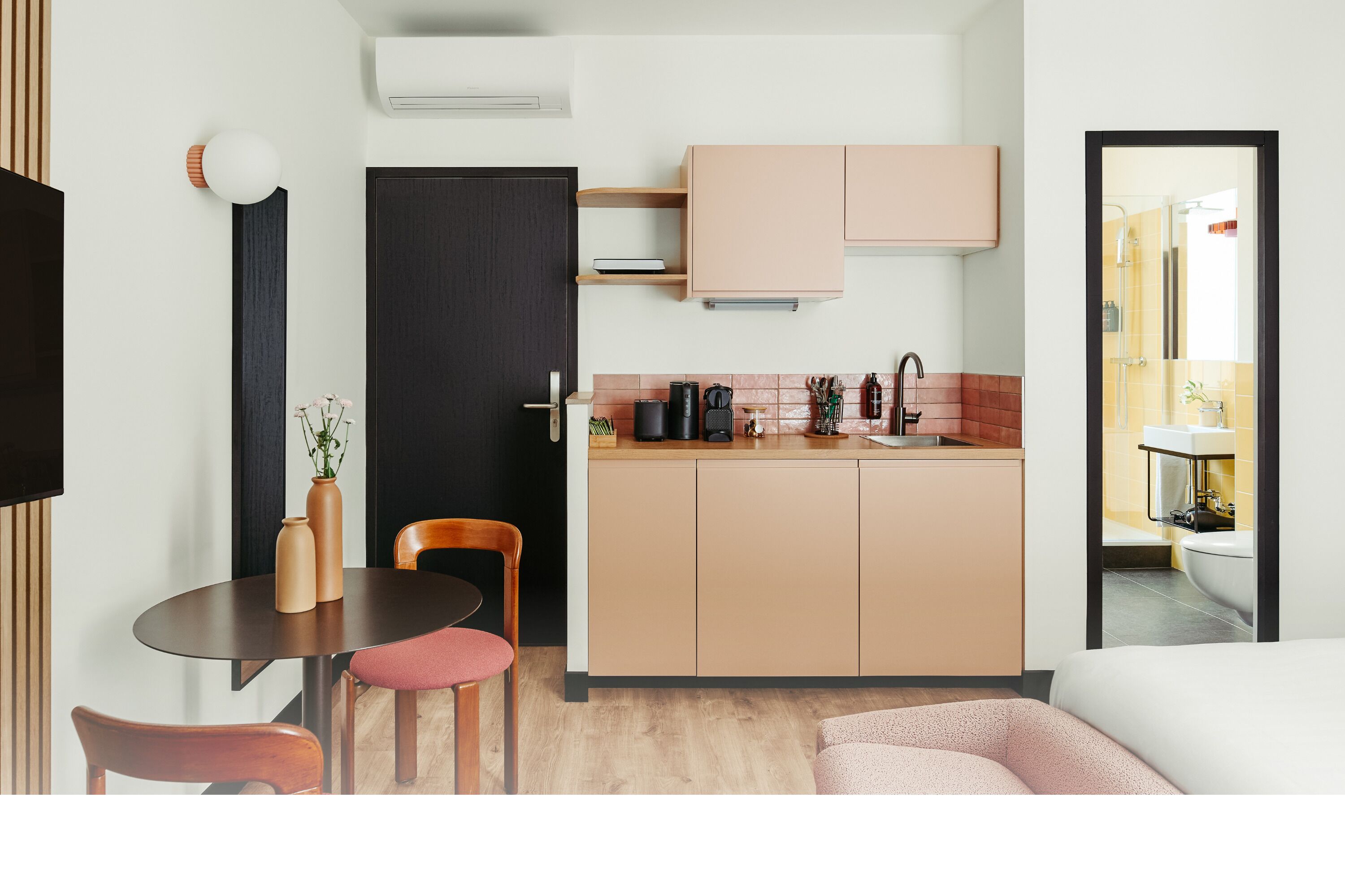 A compact kitchen with a dining area, a dark door, and a view into a bathroom.