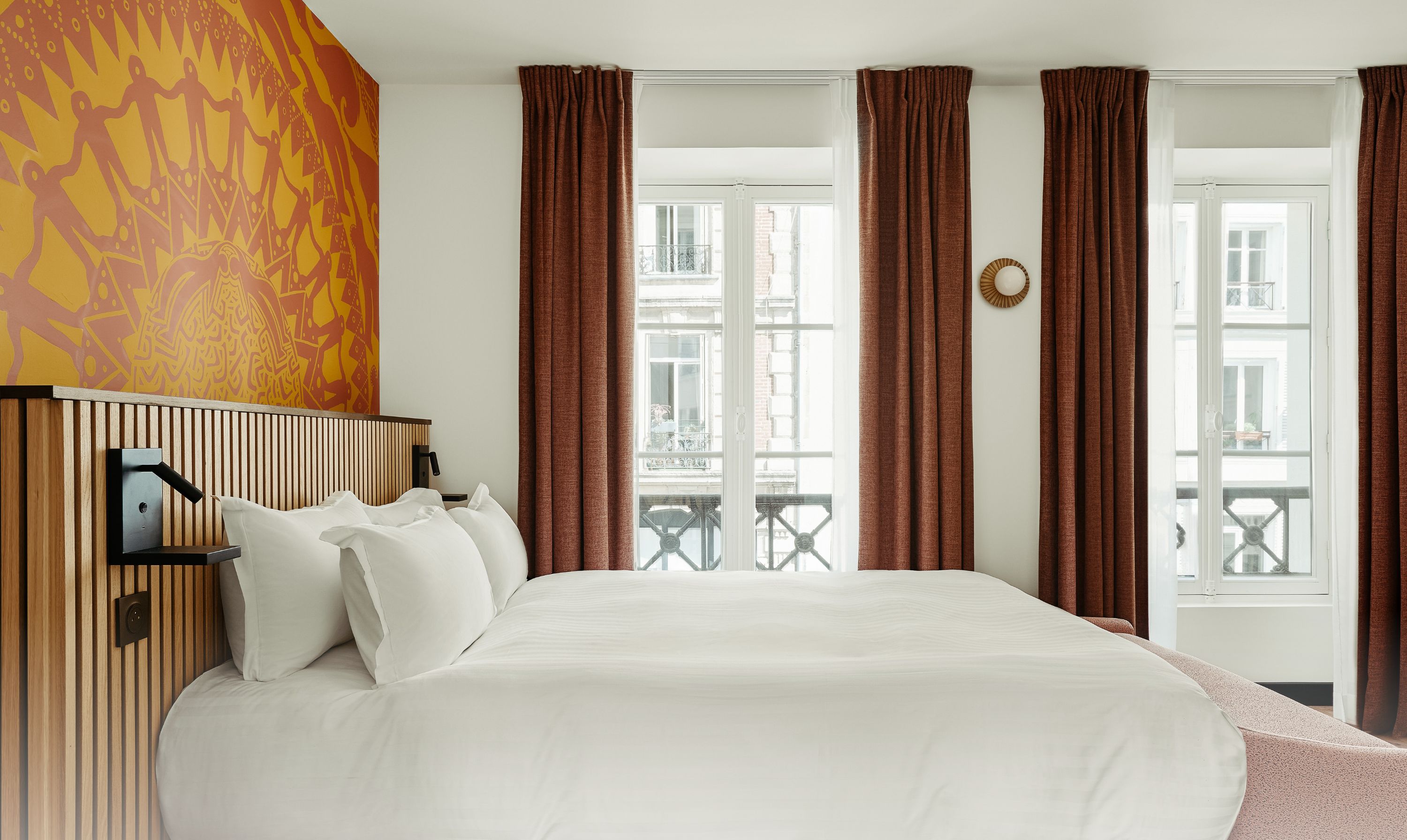 A hotel room with a large bed, a wooden headboard, a view of the city, and a balcony.
