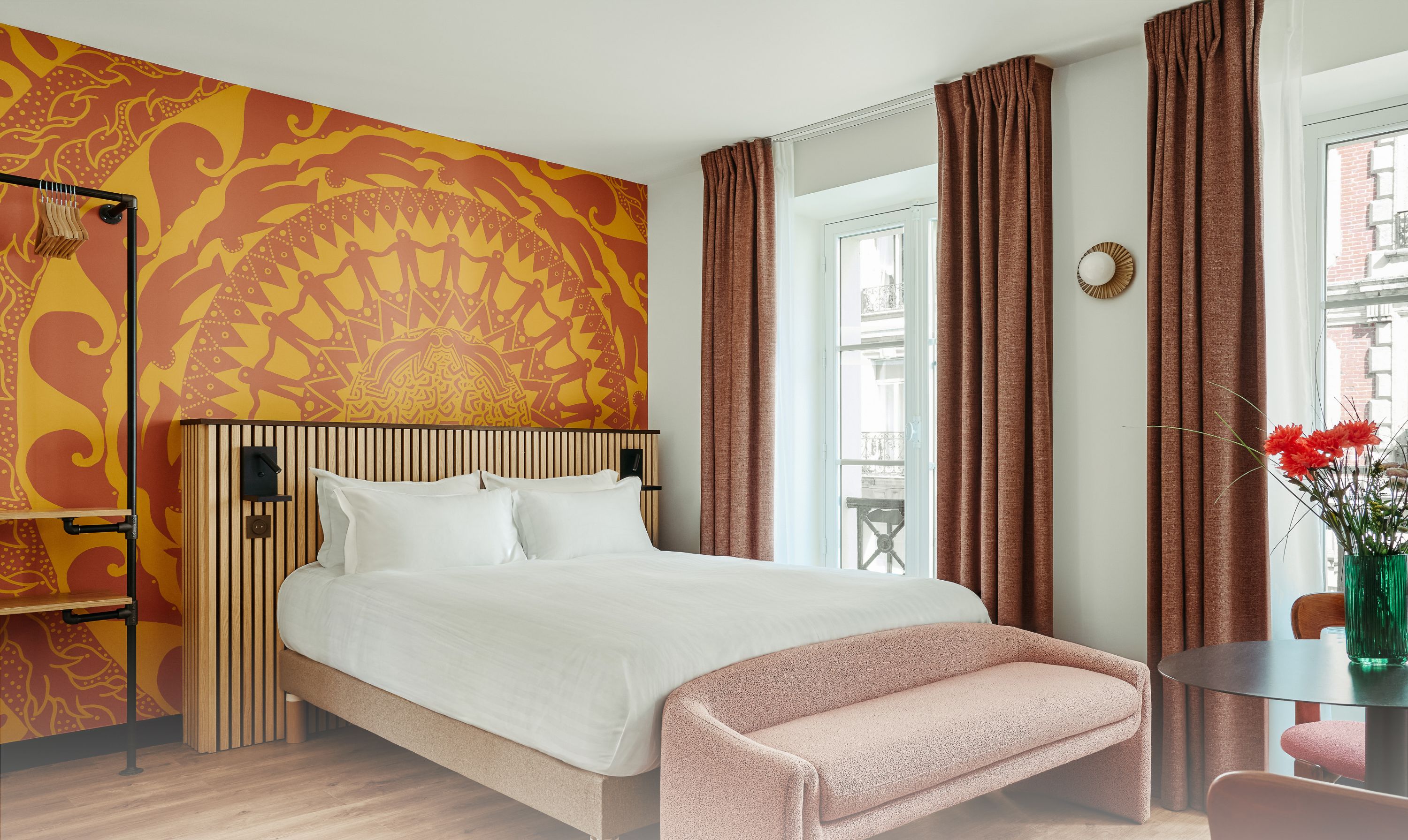 A bedroom with a bed, a bench, a table with flowers, a window, and a patterned wall. It is labeled as Apartment 23, Turenne, with 2 persons, 1 bedroom, and 1 bathroom.