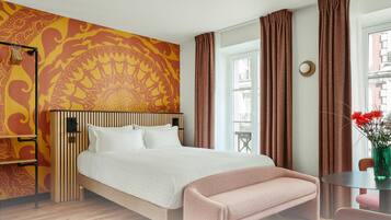 A bedroom with a bed, a bench, a table with flowers, a window, and a patterned wall. It is labeled as Apartment 23, Turenne, with 2 persons, 1 bedroom, and 1 bathroom.