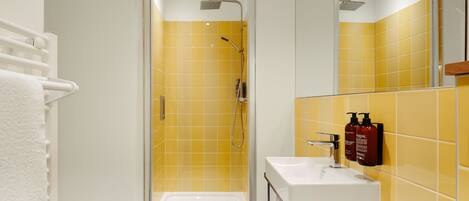 A bathroom with yellow tiles, a white sink, and a glass-enclosed shower.