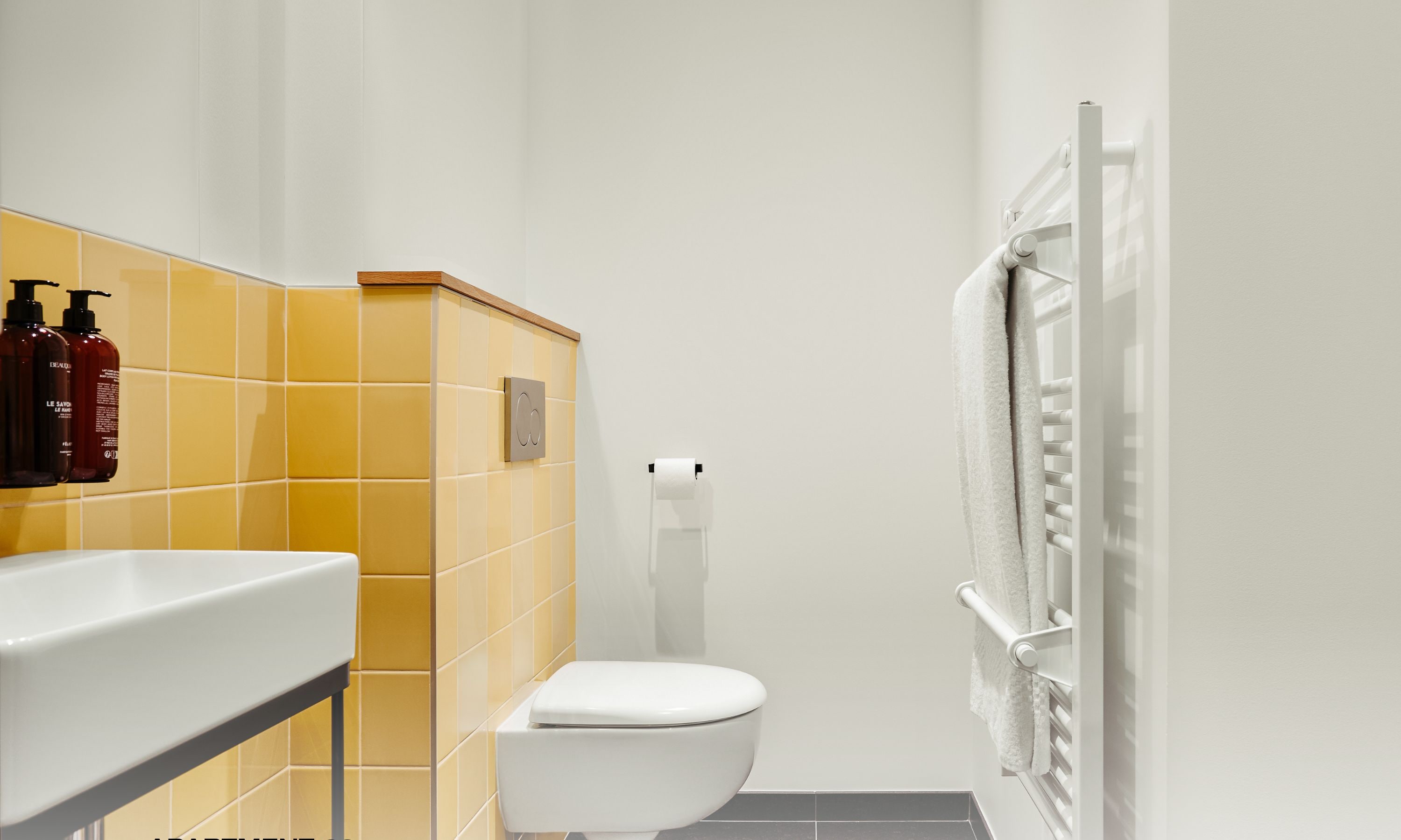 A modern bathroom with yellow tiles, a white toilet, and a towel rack.