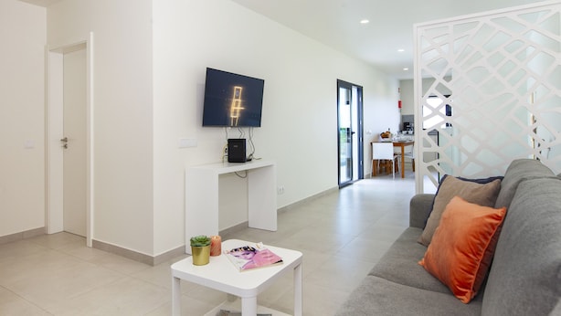 A modern living room with a grey sofa, a white coffee table, and a flat-screen TV mounted on the wall. - Villa Del Pescador (Albufeira)