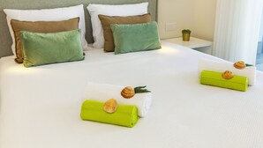 A neatly made bed with pillows and a towel, a small potted plant, and a wall-mounted light fixture. - Villa Del Pescador (Albufeira)