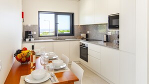 A modern kitchen with white cabinets, a granite countertop, and a dining area with a wooden table set for two. - Villa Del Pescador (Albufeira)