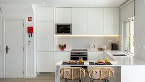 Une cuisine moderne avec des meubles blancs, un four à micro-ondes encastré et un coin repas avec deux chaises en osier.