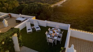 Une terrasse sur le toit, avec une table et des chaises, d’où l’on peut admirer un paysage côtier avec des arbres et un sentier.