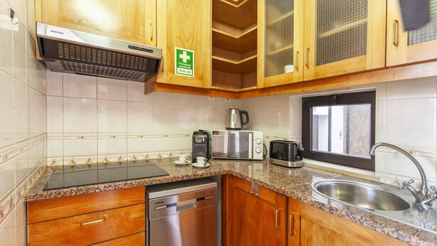 Uma cozinha com armários de madeira, pia de aço inoxidável, lava-louças, cafeteira, torradeira e micro-ondas.