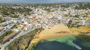 Vista aérea de uma cidade costeira com praia de areia, águas azuis cristalinas e um litoral rochoso.