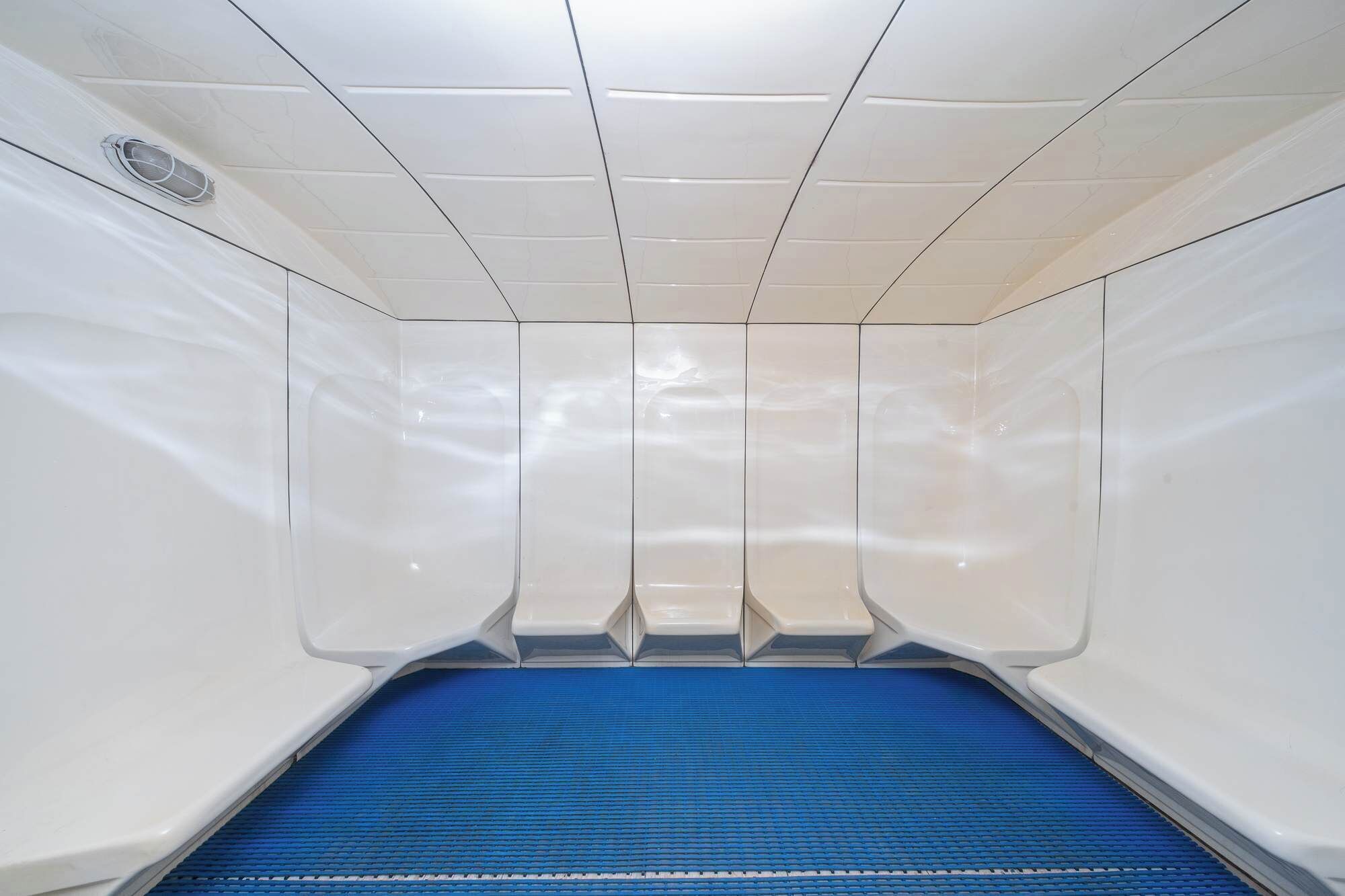 Una habitación con un tapete azul en el suelo, paredes blancas y un sistema de ventilación en el techo.