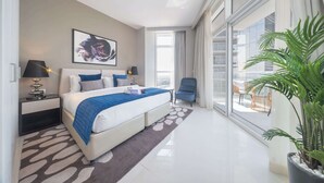 A modern hotel room with a large bed, a nightstand, a chair, and a balcony with plants. - StayShort - Damac Hills cozy studio for 2 people! (Damac Hills)