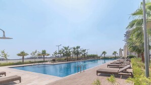 A swimming pool with lounge chairs and palm trees. - StayShort - Damac Hills cozy studio for 2 people! (Damac Hills)