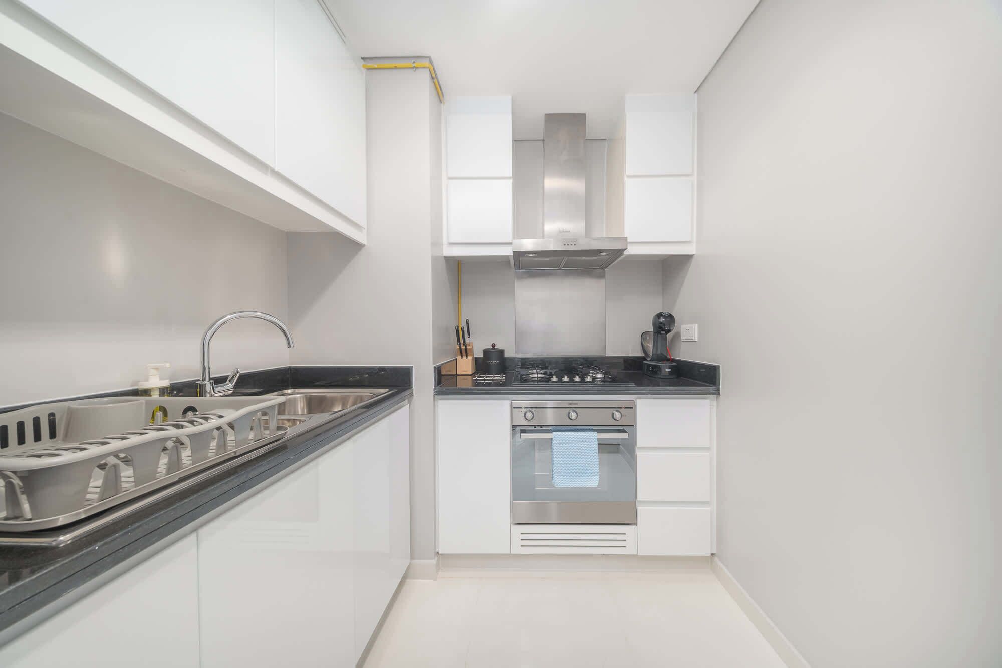 Une cuisine compacte avec des meubles blancs, un évier en acier inoxydable, une cuisinière et une hotte aspirante.