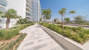 A modern building with a long, straight pathway lined with greenery and palm trees. - StayShort - Damac Hills cozy studio for 2 people! (Damac Hills)