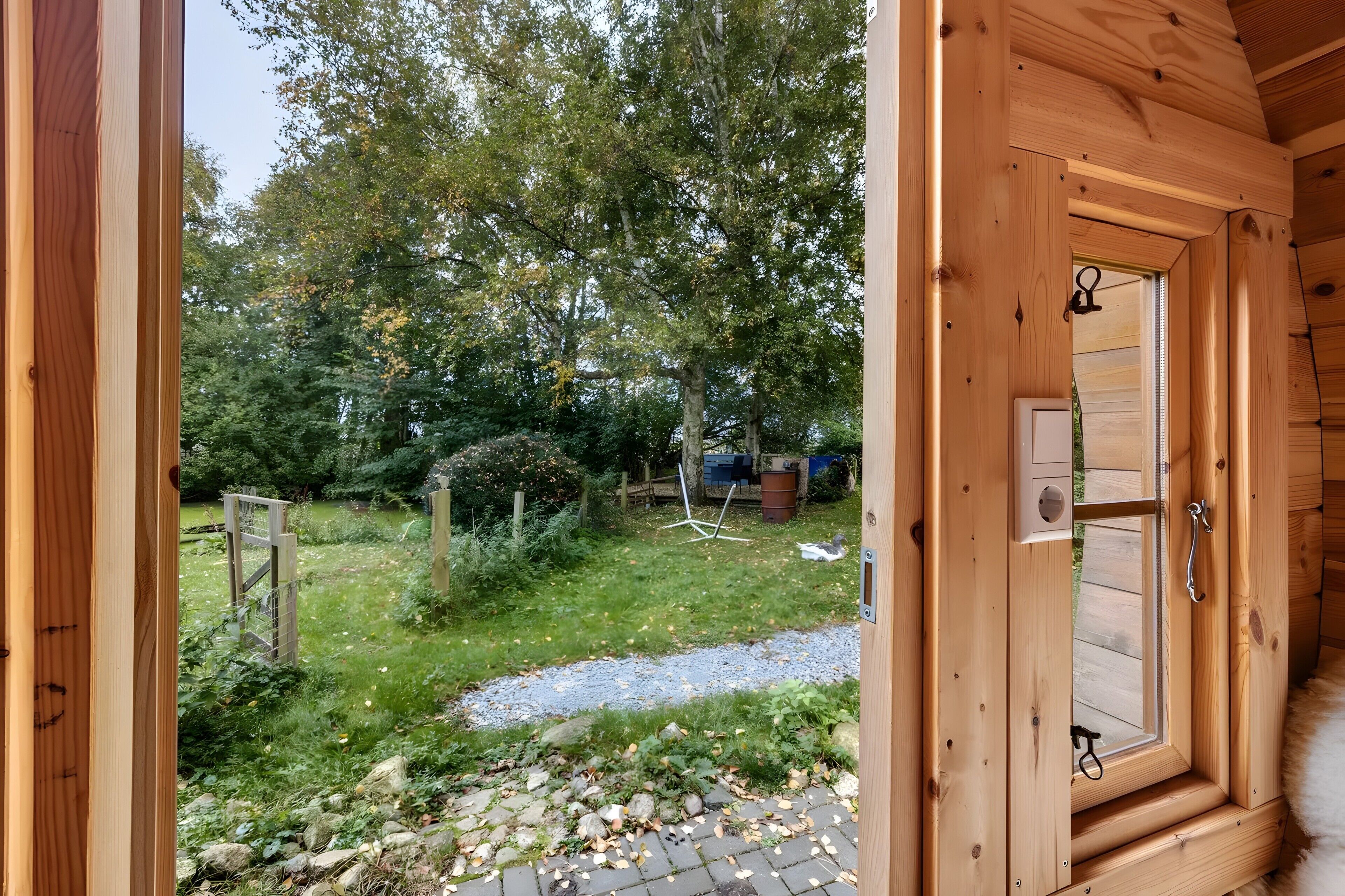 A wooden door leading to a garden with a gravel path, trees, and a wooden fence.