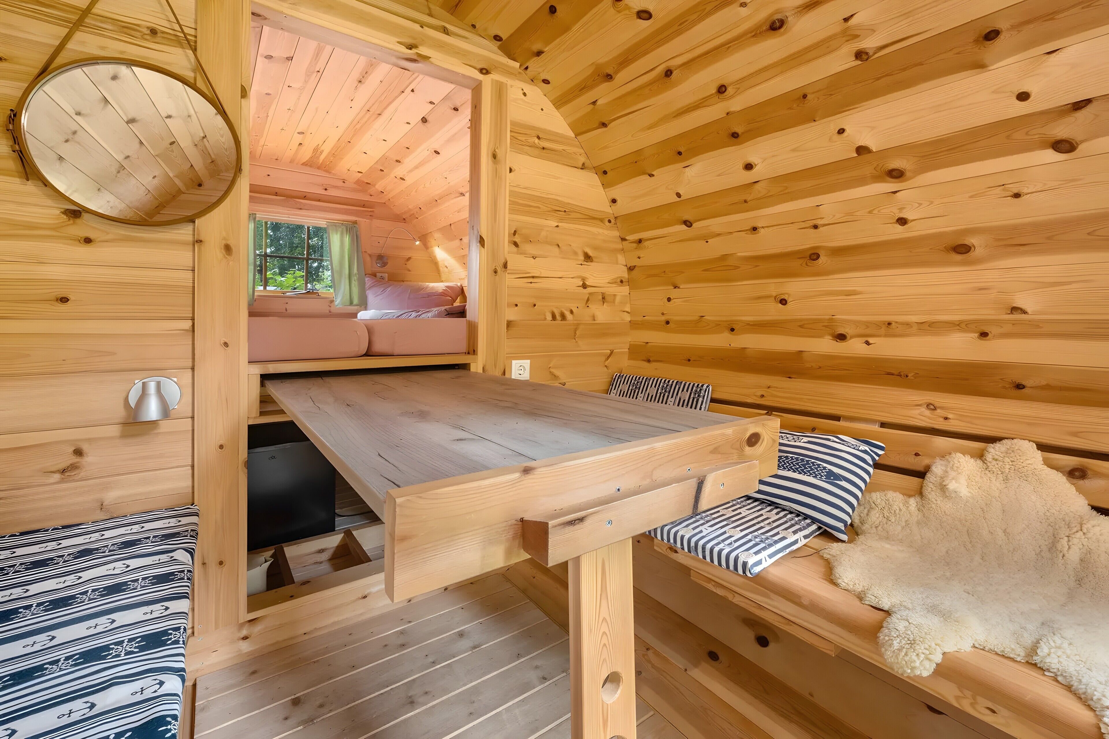 A wooden cabin interior with a bunk bed, a dining table, and a fur rug.