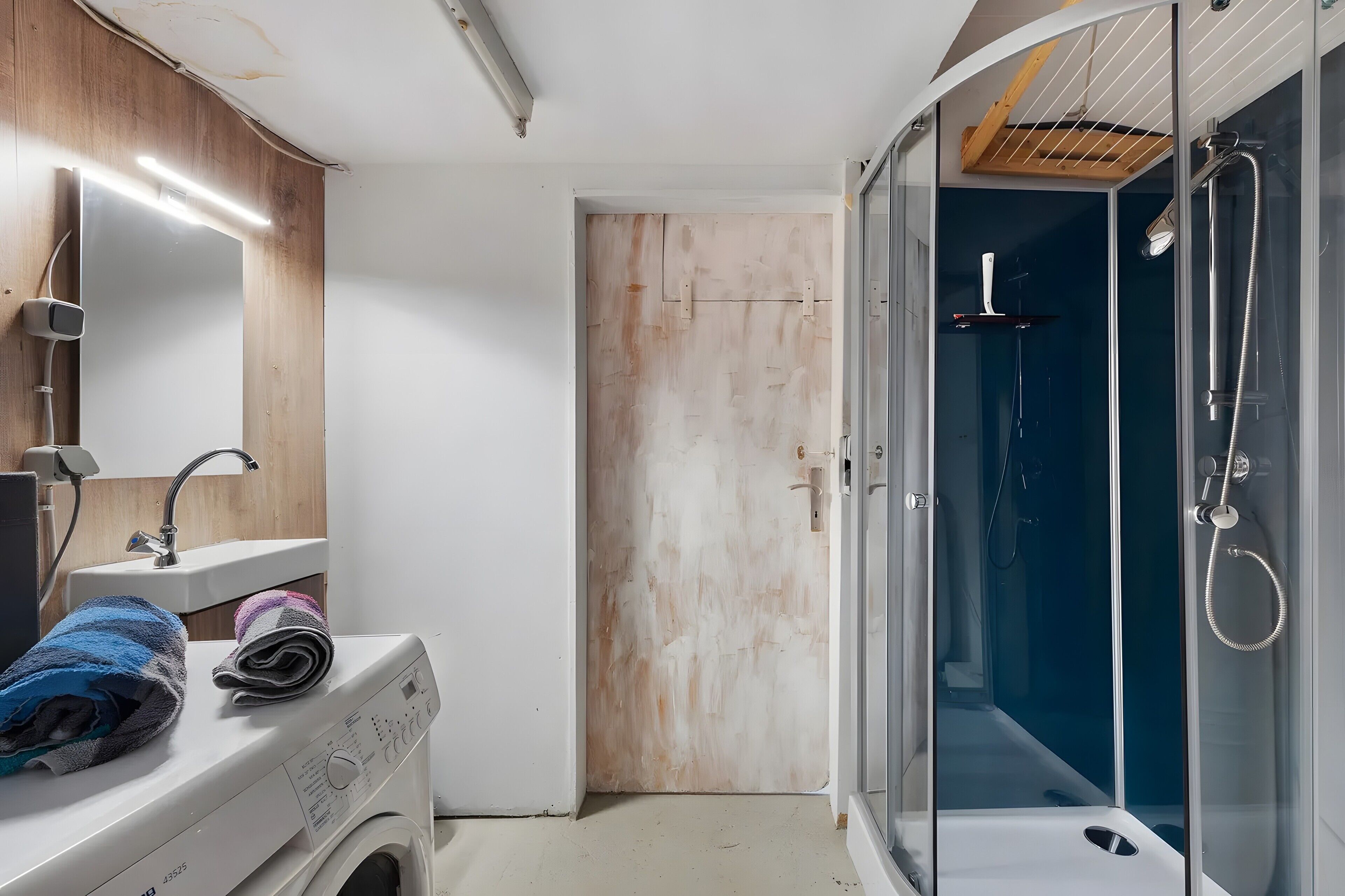 Une salle de bain équipée d’un lave-linge, d’un évier, d’un miroir et d’une douche à parois en verre.