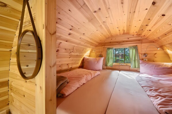 Acogedora habitación de cabaña con cama, ventana con cortinas y techo de madera.