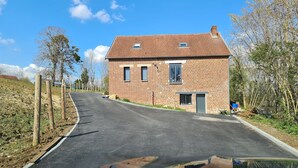 A single-story brick house with a sloped roof, a small attached garage, and a paved driveway. - Maison de Guise, pets welcome (Guise)