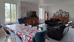 A living room with a dining area, a stone wall, a television, and artwork on the wall. - Maison de Guise, pets welcome (Guise)