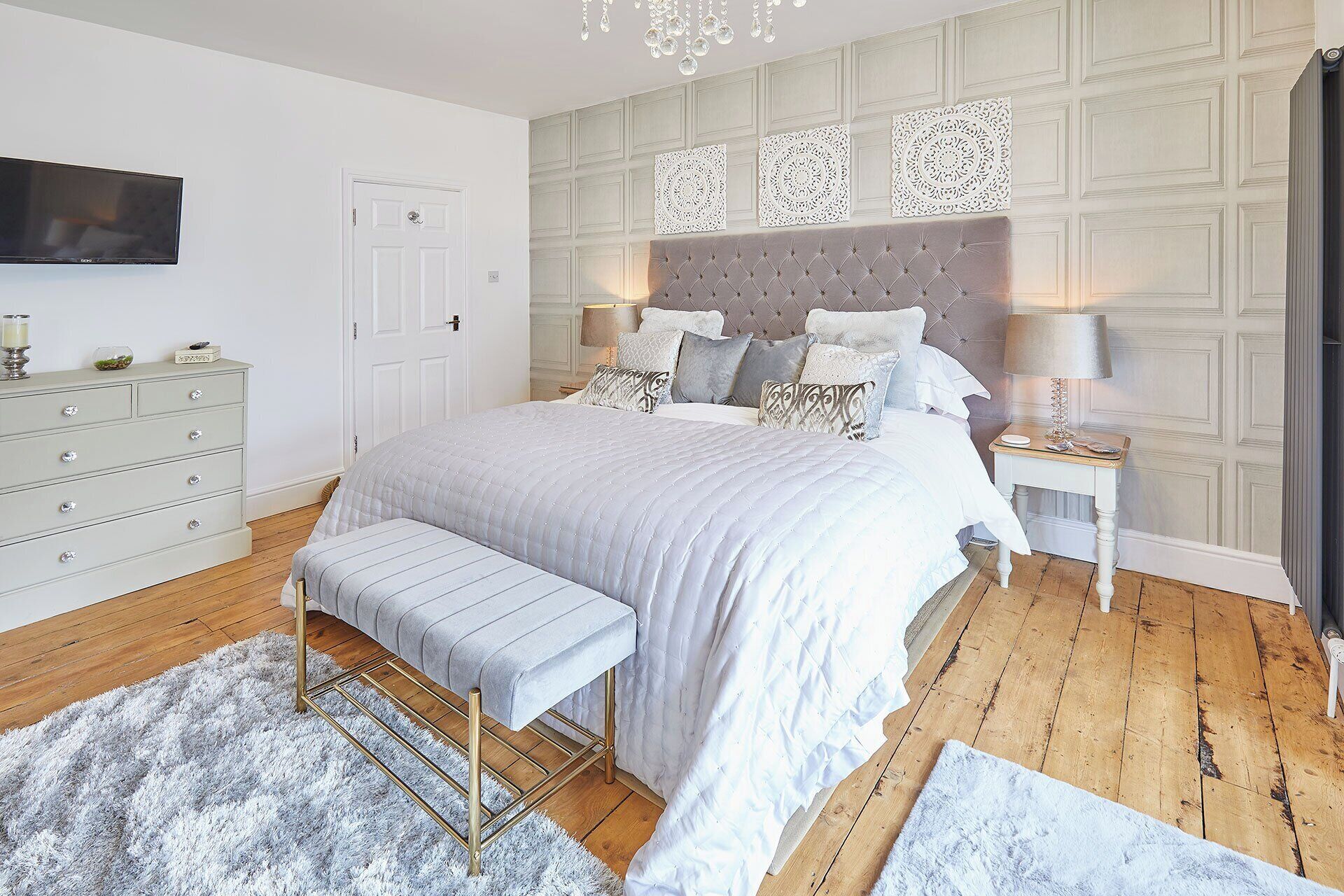 A bedroom with a large bed, a bedside table with a lamp, a dresser, and a television on the wall.