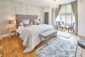 Une chambre à coucher avec un grand lit, un banc, deux chaises, une petite table et un lustre.