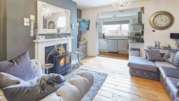 A living room with a fireplace, sofa, and a kitchen in the background.