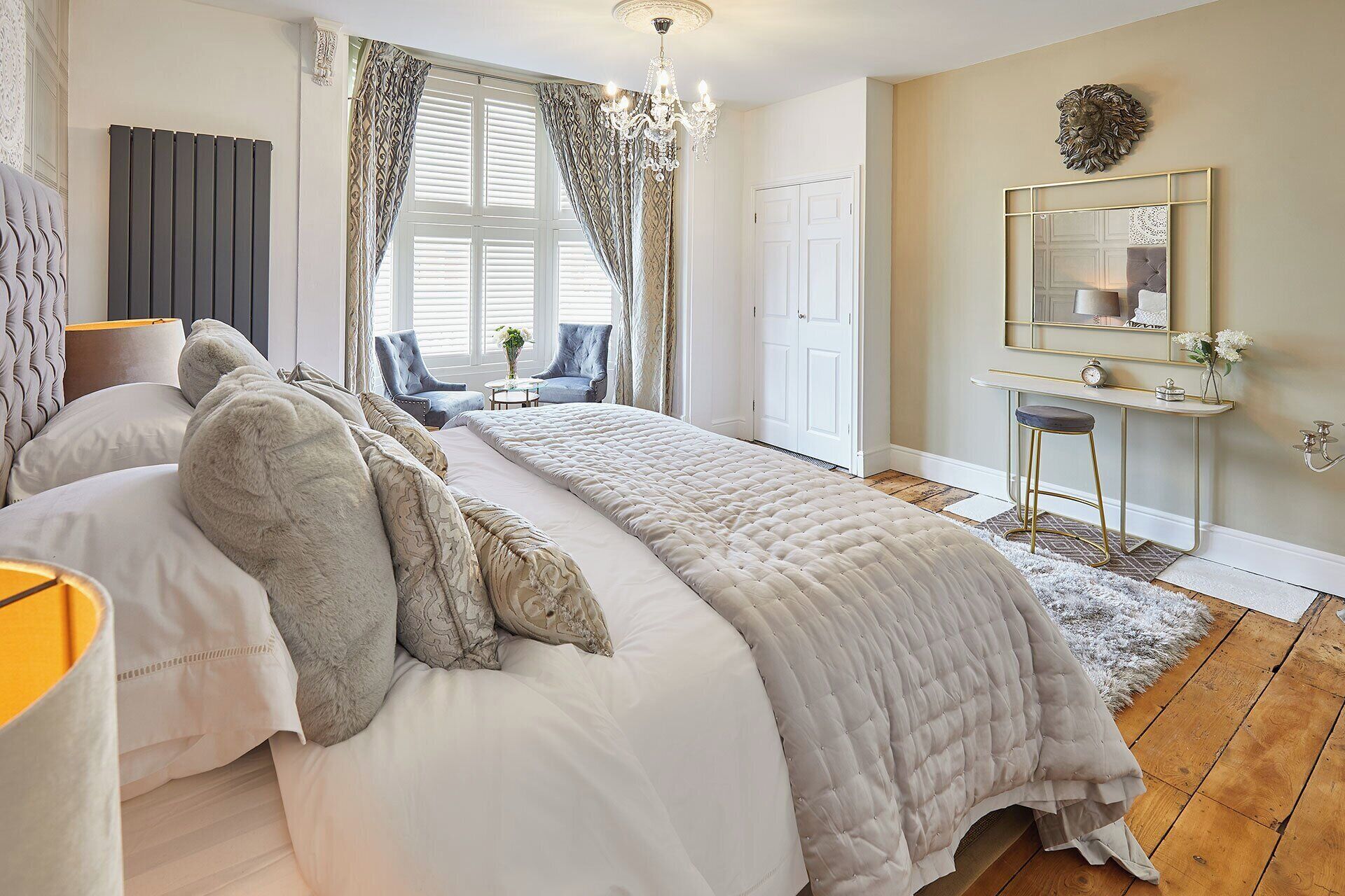 A bedroom with a large bed, a desk, a chair, a mirror, and a chandelier.