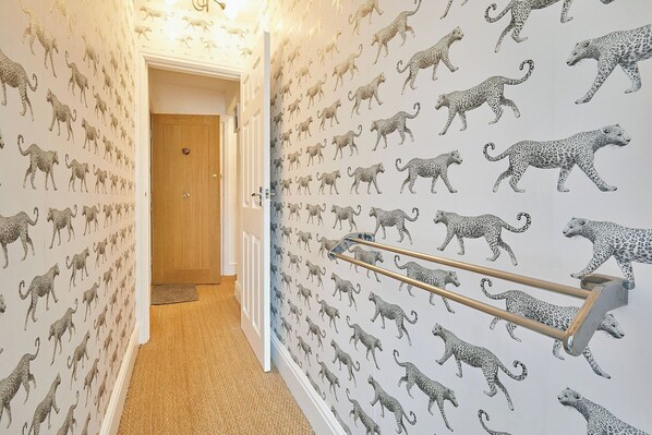 Un couloir avec un papier peint à motifs léopard, une porte en bois et un étagère en métal.
