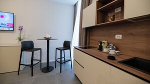 A compact kitchen with a wooden countertop, two bar stools, a small table with candles, and a potted orchid. - Imperium Suite Trevi (Rome)