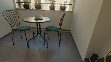 A small balcony with a round table and two chairs, potted plants on the windowsill, and a decorative item on the floor.