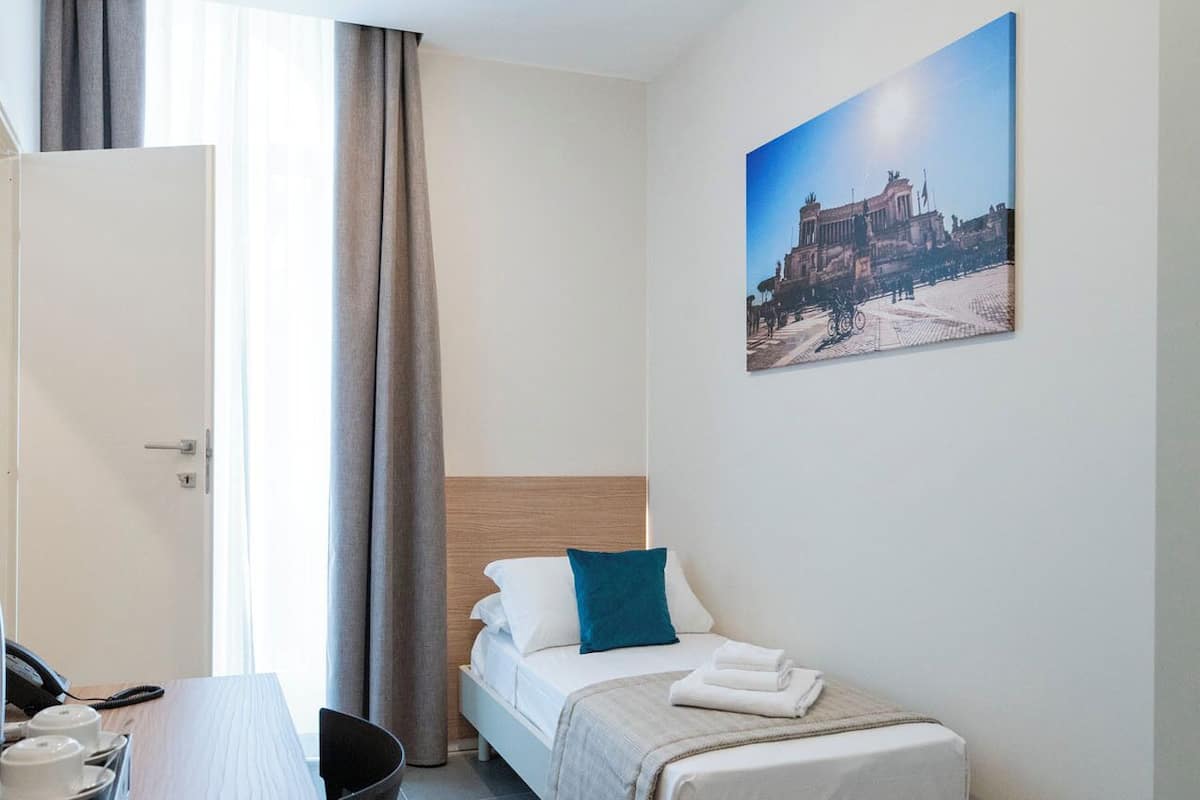Une chambre d’hôtel de taille réduite, comprenant un lit, un bureau avec un téléphone et une chaise.