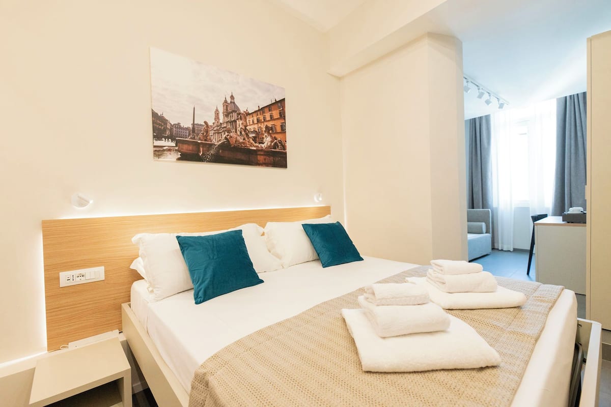 Une chambre d’hôtel avec un lit, une tête de lit, un tableau représentant un paysage urbain, un bureau et une chaise.