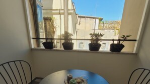A round table with two chairs, a window with potted plants, and a view of buildings outside. - Imperium Suite Trevi (Rome)