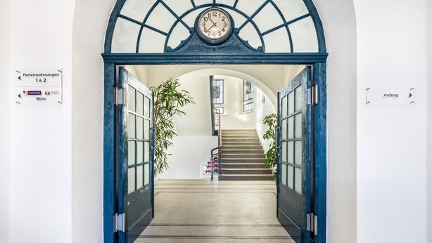 L’entrée d’un hôtel, avec une horloge, un escalier et des panneaux d’indication.