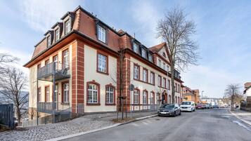 A multi-story building with a red and beige facade, a cobblestone street, and parked cars.
