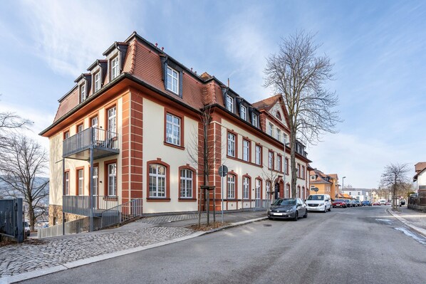 Ein mehrstöckiges Gebäude mit roter und beiger Fassade, eine Kopfsteinpflasterstraße und geparkte Autos.