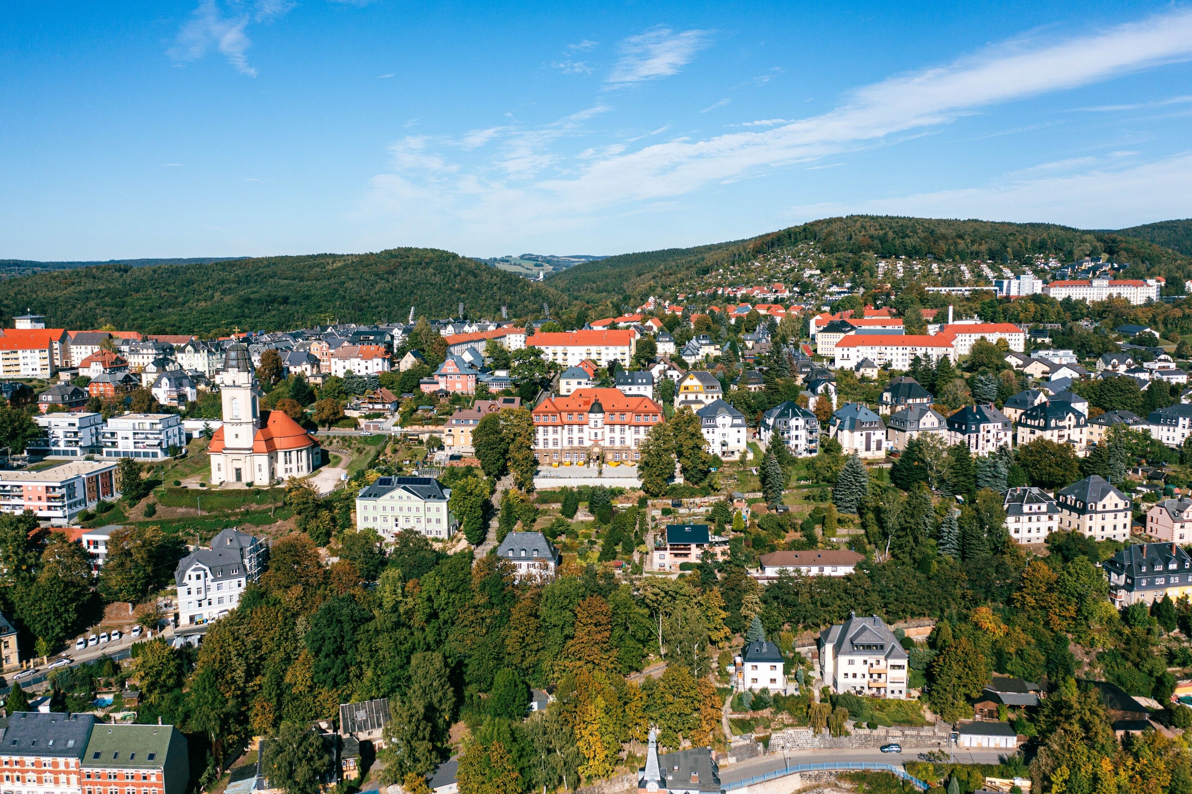 A town with a mix of residential and historical buildings, surrounded by hills and greenery.