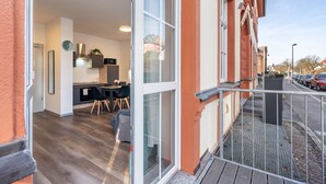 Une entrée ouverte donnant sur un appartement moderne, avec une cuisine, un coin repas et un balcon doté d’une rambarde en métal.
