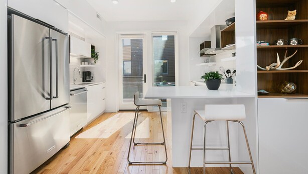 A modern kitchen with white cabinetry, stainless steel appliances, and a bar area with stools. - The Overlook | Luxe Old Town Condo w/ King Suite (Fort Collins)