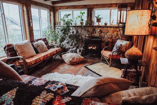 A cozy living room with a stone fireplace, wooden beams, and large windows. - Boho Art cottage in hip Bay View, Milw neighborhood- 3bed, Sauna, Hot Tub (Milwaukee)