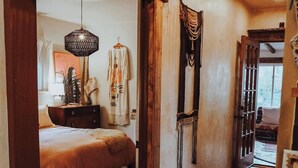 Une chambre confortable avec un lit, une tête de lit en bois, un luminaire suspendu et une vue sur une autre pièce.