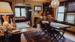 Un salon chaleureux avec une cheminée, un coin repas avec une table et des chaises en bois, et une bibliothèque remplie de livres et d’objets décoratifs.