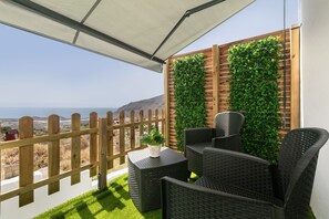 A balcony with wicker furniture, a wooden fence, and a green wall.