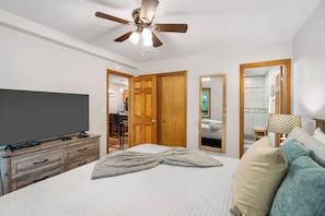 Une chambre à coucher avec un lit, un téléviseur posé sur une commode en bois, un ventilateur de plafond et un miroir.