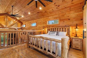 A wooden cabin bedroom with a bed, a nightstand, a lamp, and a ceiling fan.