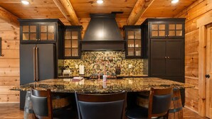 A kitchen with a large island, dark cabinetry, and a stone backsplash.