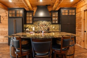A kitchen with a large island, dark cabinetry, and a stone backsplash.