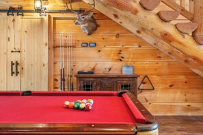 Une table de billard avec des billes, une tête de cerf accrochée au mur et des lambris en bois.